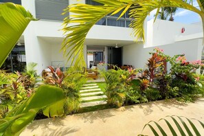 Relax in a serene outdoor space with a neatly trimmed lawn, tropical plants, and a paved pathway leading to a covered seating area.