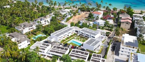 An aerial view of a coastal residential area with modern buildings, a swimming pool, and a clear view of the ocean.