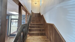 A wooden staircase with a black railing, leading up to a room with a chandelier.