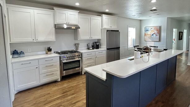 A modern kitchen with white cabinets, a central island, stainless steel appliances, and a wooden floor.