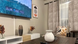 Ein modernes Wohnzimmer mit Couchtisch aus Holz, einem an der Wand montierten Fernseher, der Wetterinformationen anzeigt, und dekorativen Vasen auf einem weißen Konsolentisch.