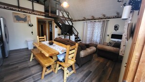 Un espacio de sala acogedor con una mesa de comedor de madera, bancos y un sofá. Una escalera conduce a un nivel superior.