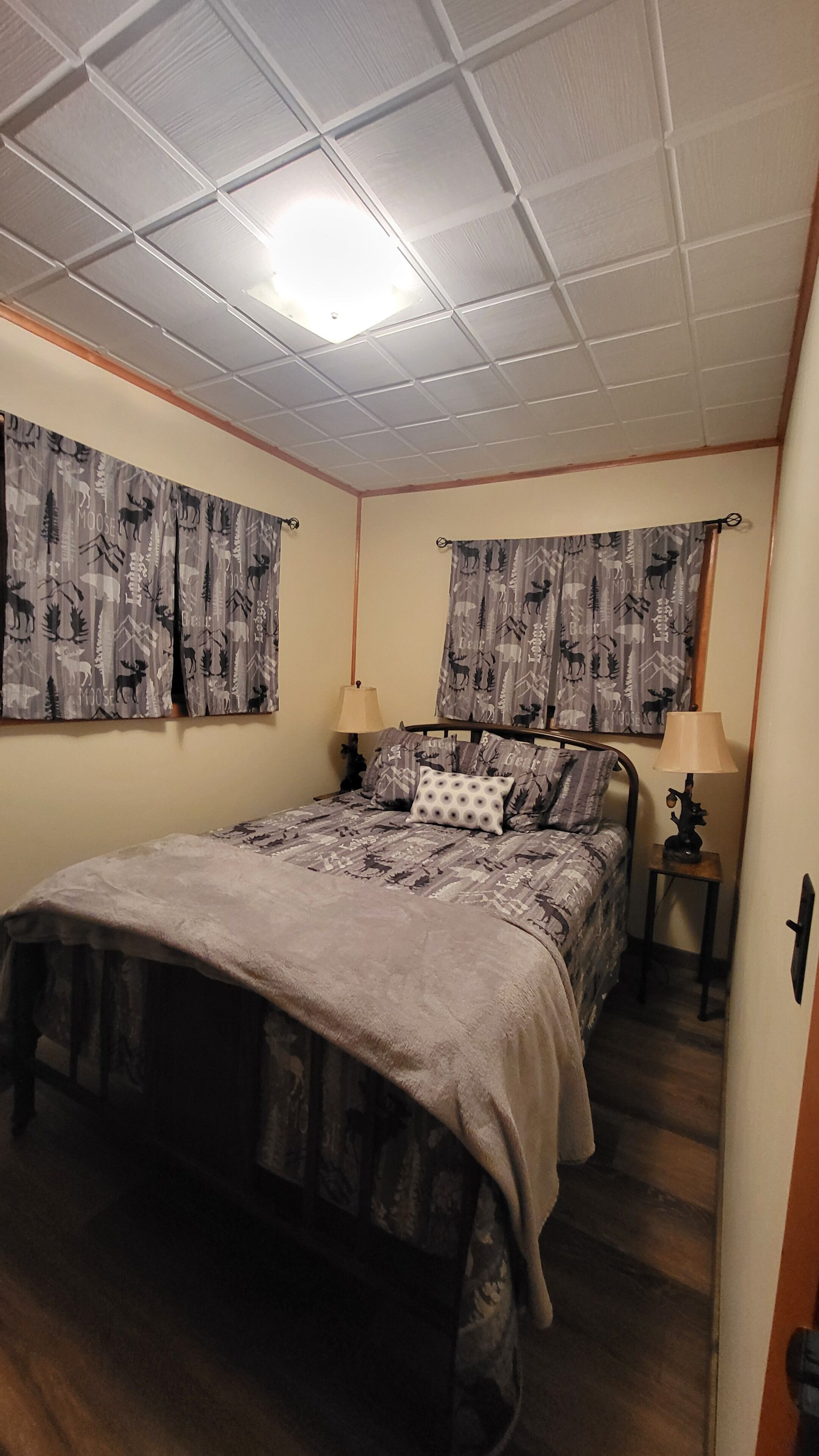 Een slaapkamer met een bed, twee nachtkastjes, een lamp op elk kastje, en gordijnen met een motief van elanden.