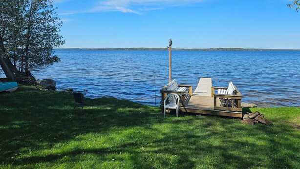 Terraza junto al lago con una silla, una mesita y una estructura de madera que tiene una silla adentro.