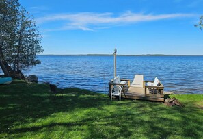 Une terrasse au bord du lac, avec une chaise, une petite table et une structure en bois abritant une autre chaise.