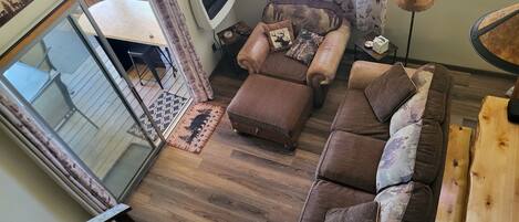 Un salon chaleureux avec un canapé en cuir marron, un pouf et un tapis à motifs.