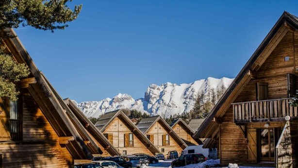 A row of wooden cabins with a mountain backdrop, featuring a clear sky and snow-covered ground. - Chalet, 150m from resort center, view mountain, swimming pool, sauna, terrace, parking, tv (Agnières-en-Dévoluy)