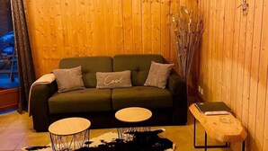 A cozy living room with a wooden wall, a green sofa, two round tables, and a cowhide rug. - Chalet, 150m from resort center, view mountain, swimming pool, sauna, terrace, parking, tv (Agnières-en-Dévoluy)
