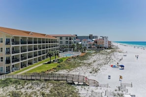 A beachfront hotel with multiple floors, a swimming pool, and a beach area with umbrellas and lounge chairs.