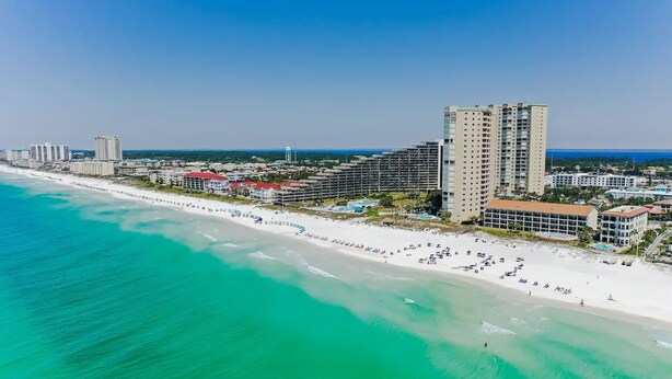 Ein Küstenhotel mit mehreren Hochhäusern, einem Strand und einem klaren, blauen Himmel.