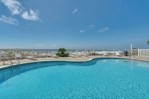 A clear blue pool with a curved edge, surrounded by white lounge chairs and a white fence.