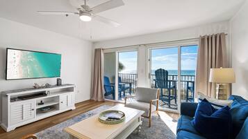 A living room with a television, sofa, coffee table, and a balcony with chairs.