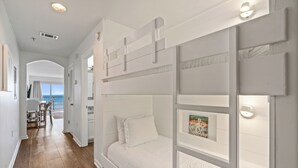 Ein Stockbett mit weißem Kopfteil und einem gerahmten Bild. Ein Holzboden und ein weißer Teppich sind zu sehen.
