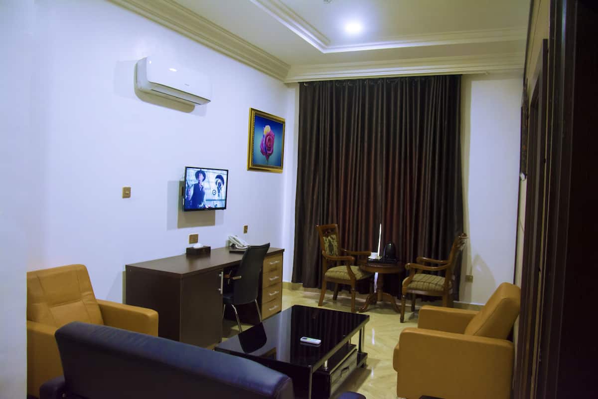 A hotel room with a flat-screen TV, a desk with a telephone, two armchairs, a coffee table, and a large window with curtains.