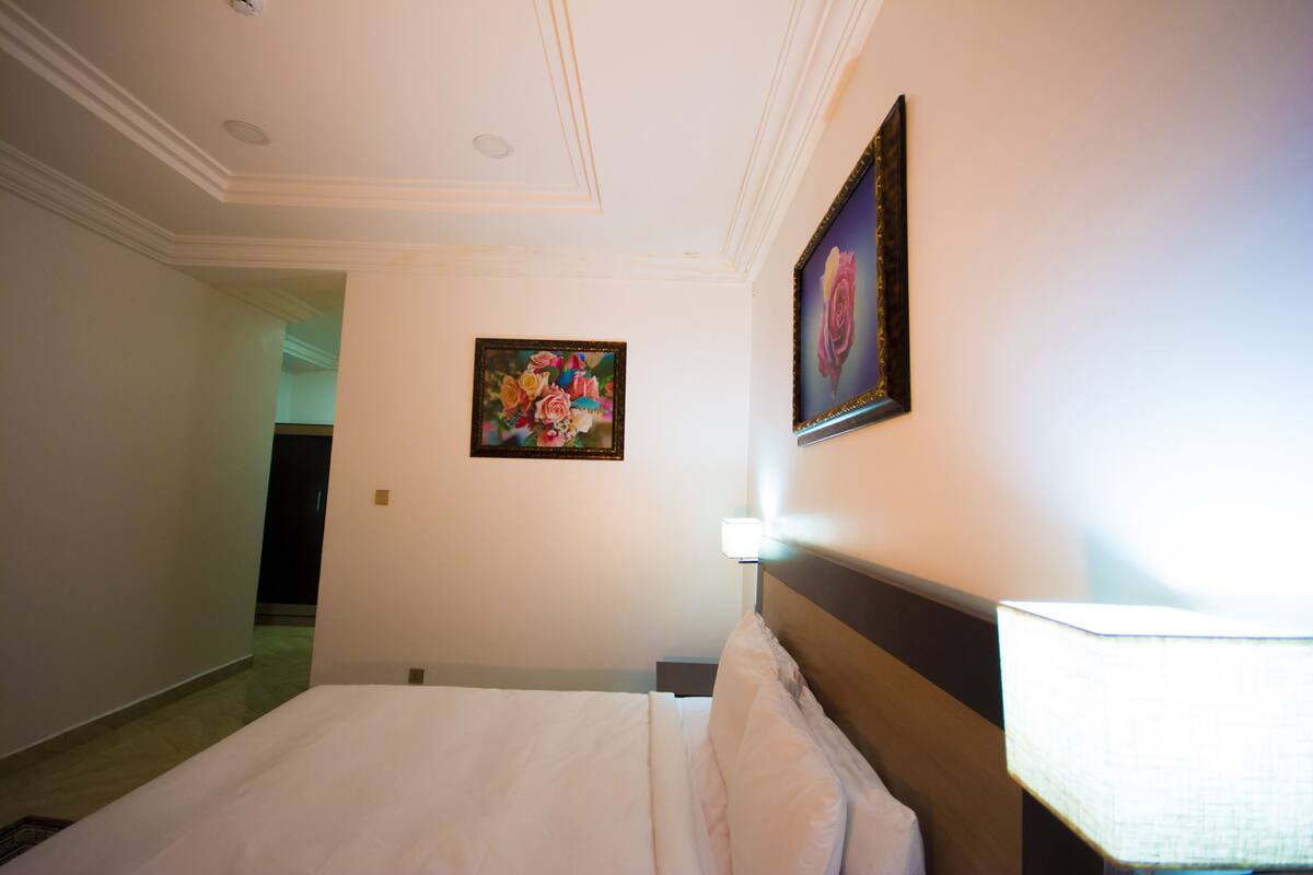 A hotel room with a neatly made bed, a wall-mounted painting, and a lamp.
