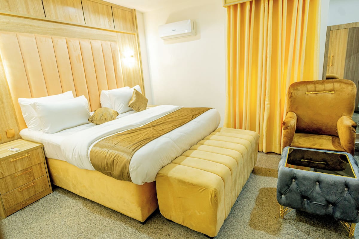 A hotel room with a large bed, a wooden headboard, a nightstand, a chair, and a small table.