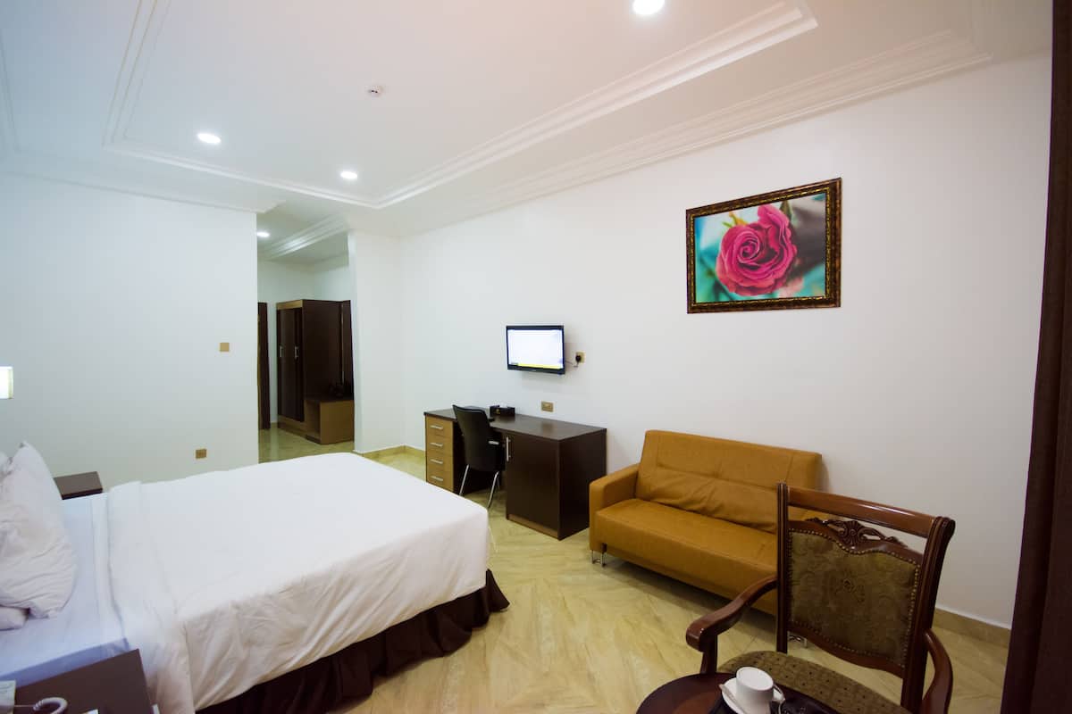 A hotel room with a bed, a desk, a sofa, a chair, and a TV on the wall.