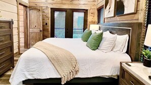 Une chambre avec un plafond en bois, un lit avec des oreillers verts et blancs, une table de chevet avec une lampe et une commode.