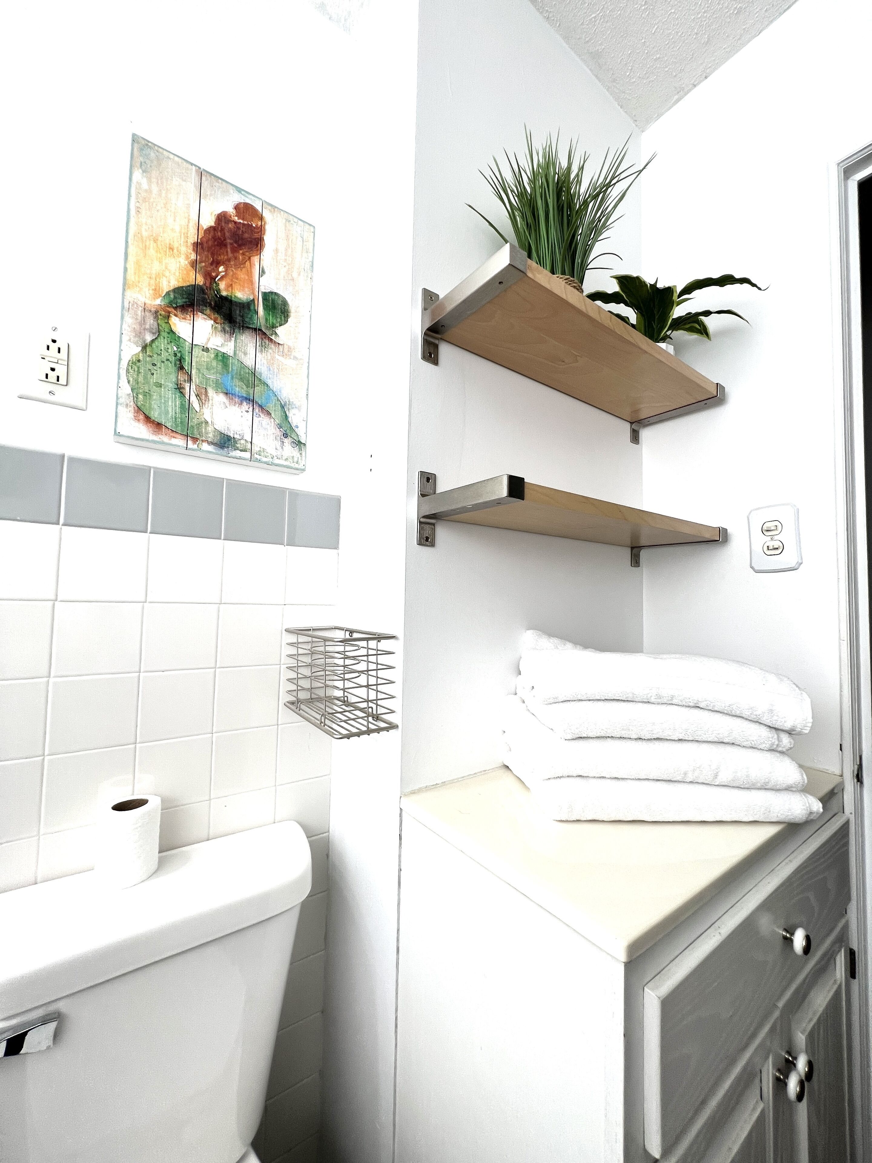 Une salle de bain comprenant des toilettes, un lavabo, un porte-serviettes et une étagère avec une plante.