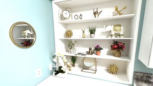 A compact, white desk with a teal accent, equipped with a small mirror, a clock, and various decorative items including figurines and plants.