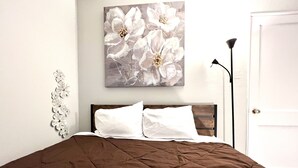 A bedroom with a bed, a painting of flowers, a lamp, and a door.