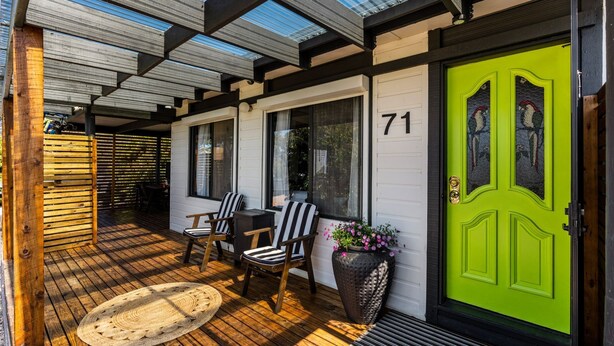 A wooden deck with two chairs and a woven mat, a bright green door with a bird painting, and the number 71 on the wall. - Inverloch' s Lime Green Door - Linen, Wifi, Pet Friendly (Inverloch)