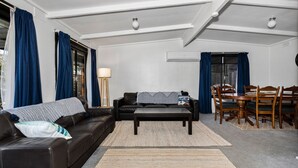 A living room with a black leather sofa, a wooden dining table with chairs, and a floor lamp. - Inverloch' s Lime Green Door - Linen, Wifi, Pet Friendly (Inverloch)