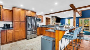A modern kitchen with wooden cabinets, stainless steel appliances, and a bar area with stools. - Sleeps 20 | Hot Tub | Game Room | Fire Pit |4500SF (Newry)
