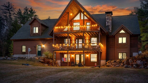 A large log cabin with a balcony, multiple windows, and a stone chimney. - Sleeps 20 | Hot Tub | Game Room | Fire Pit |4500SF (Newry)