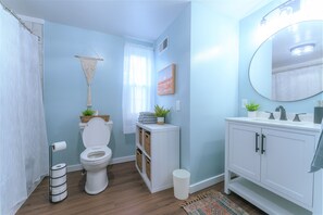 Un baño con inodoro, lavabo, espejo y una pequeña repisa con plantas.