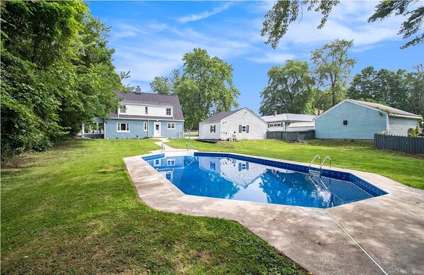 Patio residencial con piscina, una casa y árboles circundantes.
