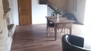 Ruime kamer met houten plafond, een eettafel met stoelen en een trap naar een hoger gelegen verdieping.