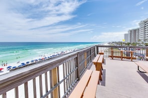 Une vue sur la plage depuis un balcon doté de balustrades en bois, d’une terrasse en bois et de parasols de plage.
