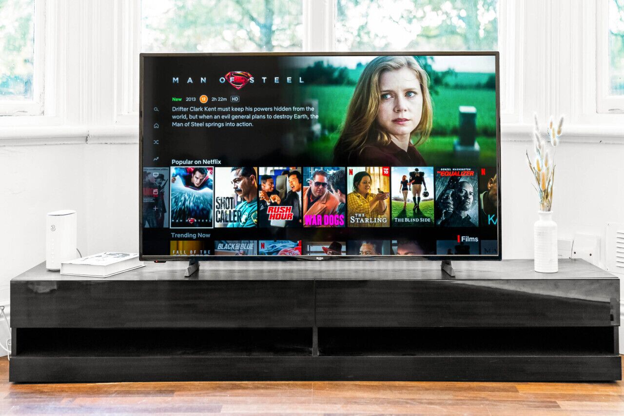 Uma sala de estar moderna com uma grande televisão de tela plana exibindo a interface de um serviço de streaming.