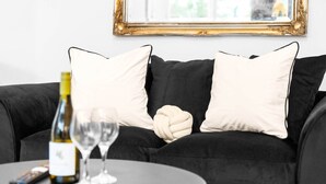 A black sofa with white cushions, a wine bottle, and two wine glasses on a round table. - Luxury Apartment - Wolverhampton (Wolverhampton)
