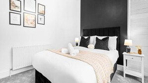 A modern bedroom with a large bed, a dark headboard, and a white nightstand with a lamp. - Luxury Apartment - Wolverhampton (Wolverhampton)