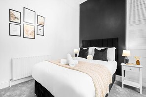 A modern bedroom with a large bed, a dark headboard, and a white nightstand with a lamp. - Luxury Apartment - Wolverhampton (Wolverhampton)