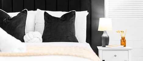 A neatly made bed with a black headboard, white and black pillows, and a white bedside table with a lamp and a small vase.