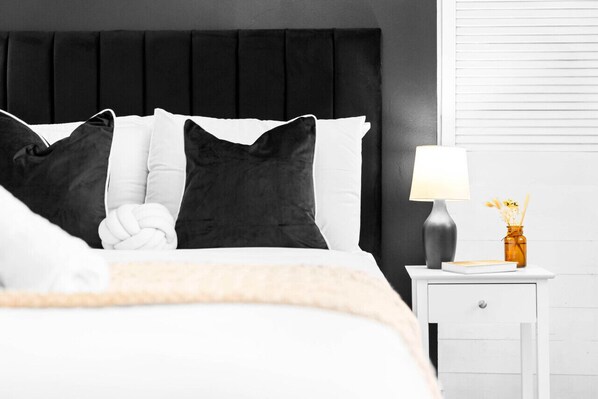 A neatly made bed with a black headboard, white and black pillows, and a white bedside table with a lamp and a small vase.