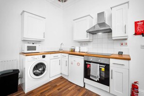 A compact kitchen with white cabinets, a microwave, a washing machine, and an oven.