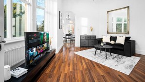 A modern living room with a large flat-screen TV, a black sofa, a coffee table, and a chandelier. - Luxury Apartment - Wolverhampton (Wolverhampton)