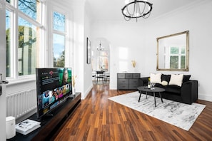 A modern living room with a large flat-screen TV, a black sofa, a coffee table, and a chandelier. - Luxury Apartment - Wolverhampton (Wolverhampton)