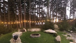 A rustic outdoor seating area with stone benches, a fire pit, and a grill.