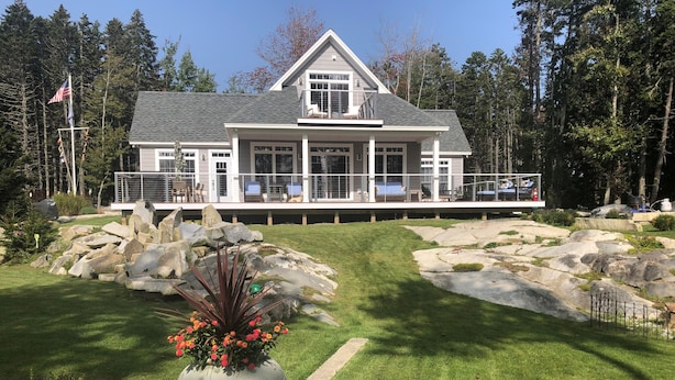 A large, modern house with a spacious deck, surrounded by a well-maintained lawn and large rocks.