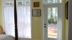 A bedroom with a four-poster bed, a large window with sheer curtains, and a door leading outside.
