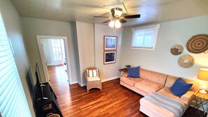 A living room with a wooden floor, a beige sofa, a wicker chair, and a ceiling fan. - Beautifully remodeled single story cottage close to downtown Cincinnati! (Dayton)