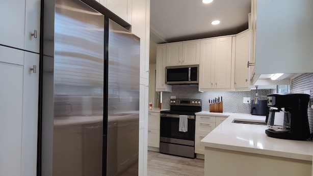 A modern kitchen with white cabinets, stainless steel appliances, and a tiled backsplash. - Beautifully remodeled single story cottage close to downtown Cincinnati! (Dayton)