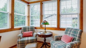 A corner room with two plaid armchairs, a small round table with a stained glass lamp, and large windows with blinds. - Historic District Home - Walk to Willapa Bay! (Oysterville)