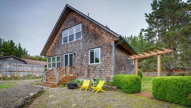 A wooden house with a stone patio, two yellow chairs, and a wooden pergola. - Historic District Home - Walk to Willapa Bay! (Oysterville)