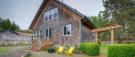 A wooden house with a stone patio, two yellow chairs, and a wooden pergola.